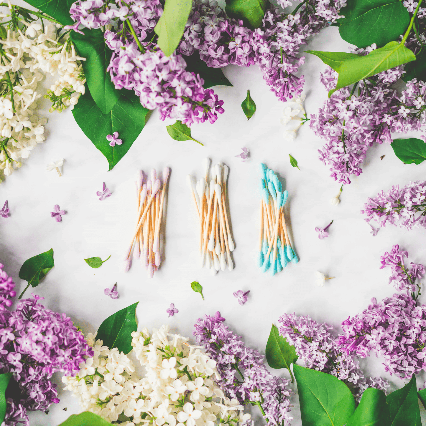 Piles of pink, white, and blue bamboo cotton swabs in the middle of a background of flowers