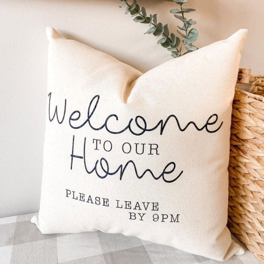 Light beige pillow that says "welcome to our home please leave by 9PM"